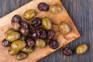 Olive verdi e nere marinate con spezie servite su tagliere in legno rustico.
